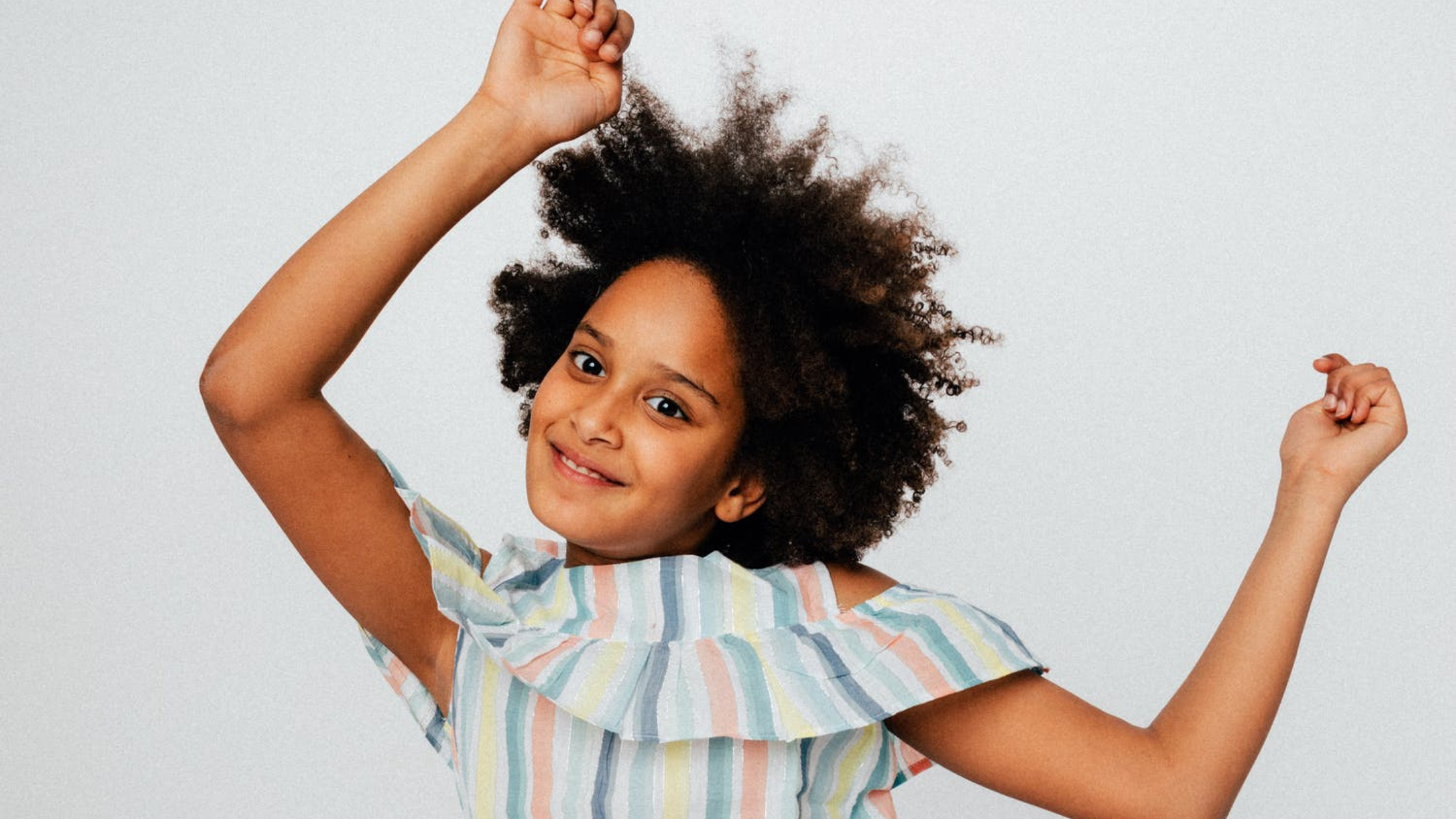 A young African American girl smiles at the camera wither her hands in the air